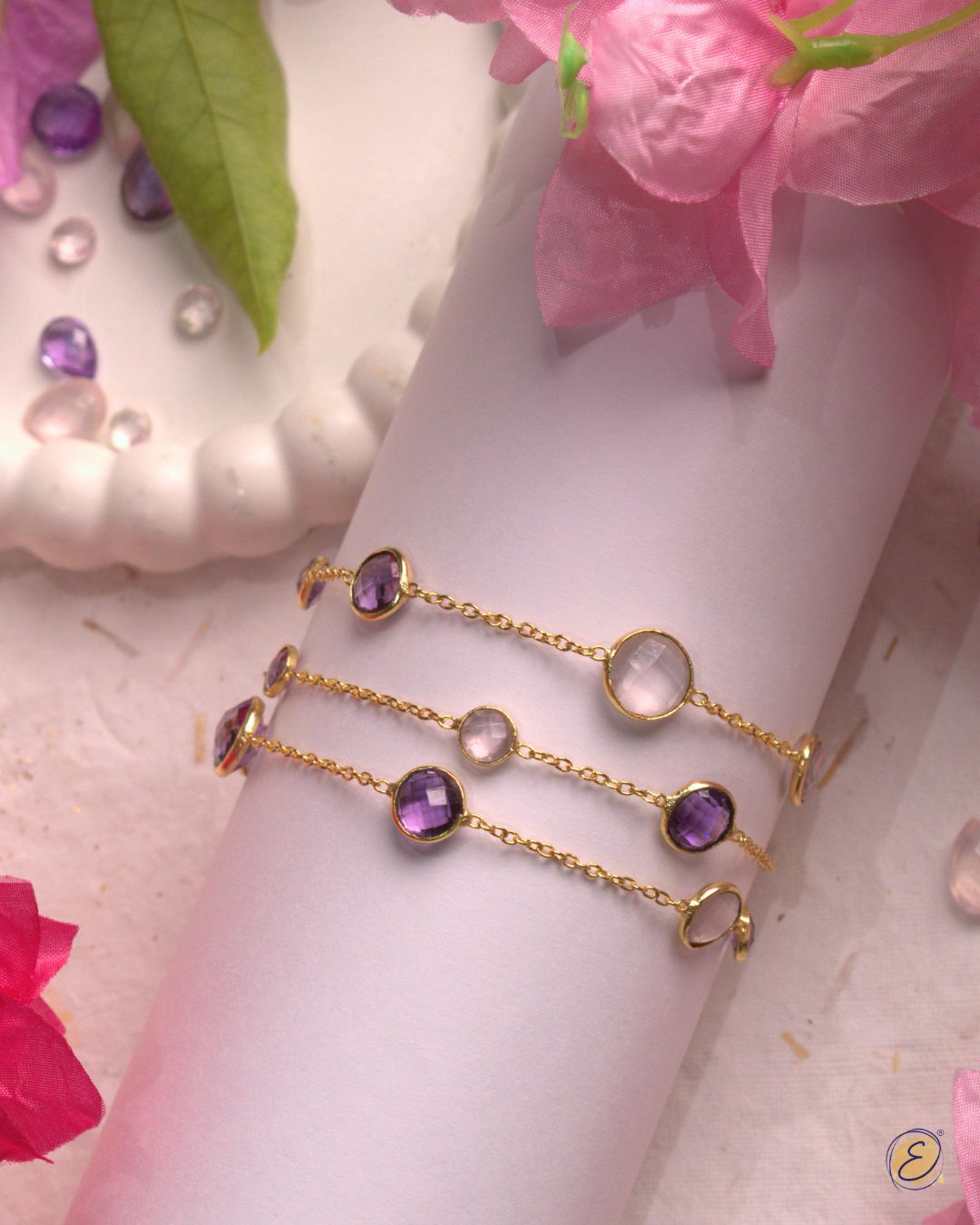 Gold bracelet and ring with gemstones on a wrist against a pink background