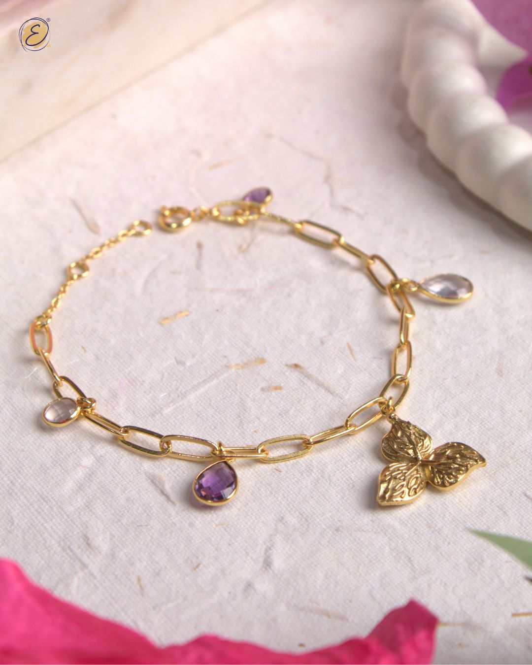 Gold-plated Kyna charm bracelet with bougainvillea charm, rose quartz & amethyst stones, handcrafted in Jaipur.