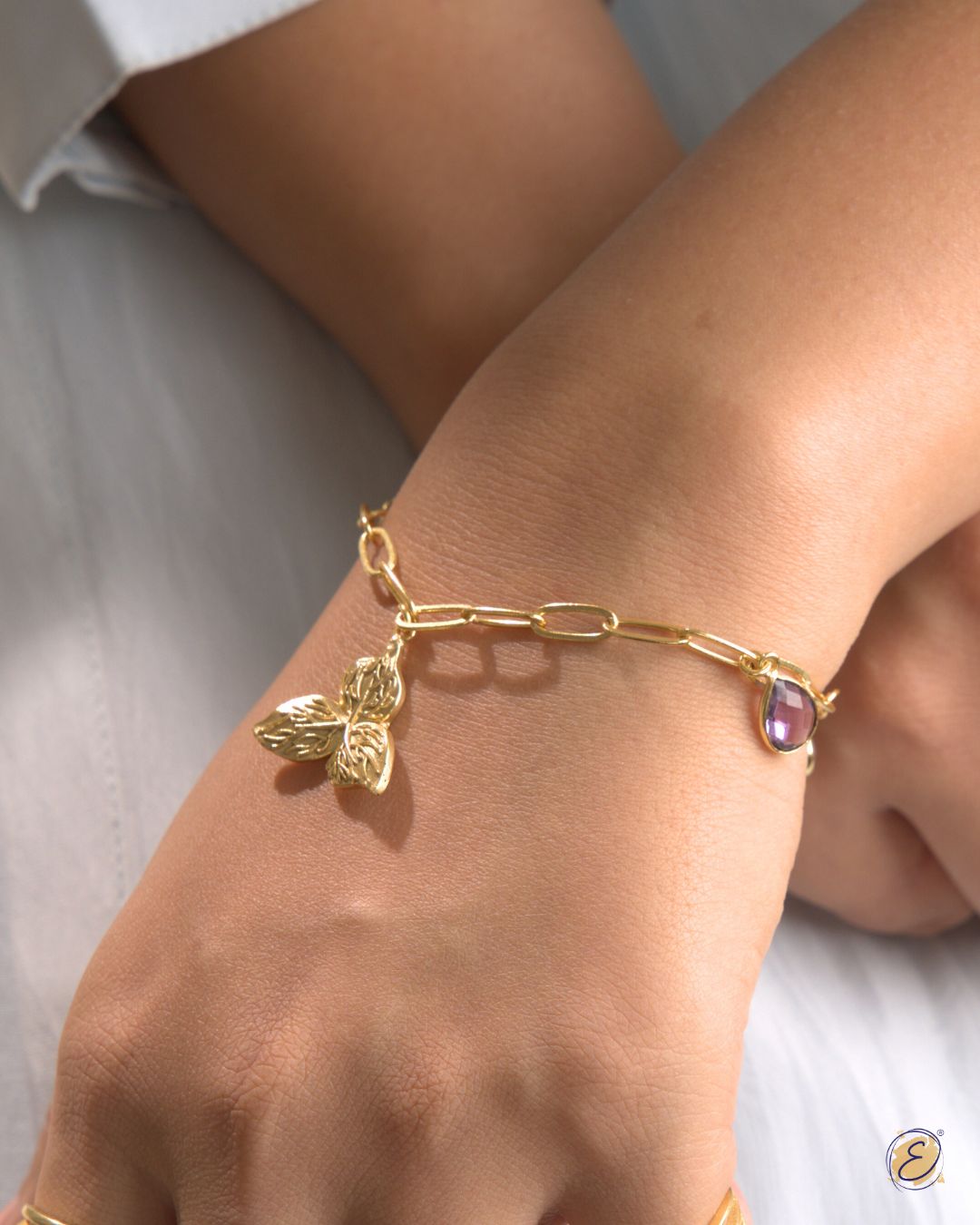 Gold-plated Kyna charm bracelet with bougainvillea charm, rose quartz & amethyst stones, handcrafted in Jaipur.